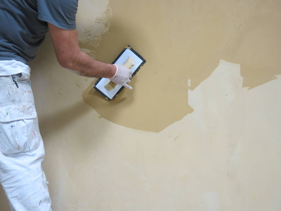 Professionnel appliquant du béton ciré sur un mur avec une truelle en caoutchouc