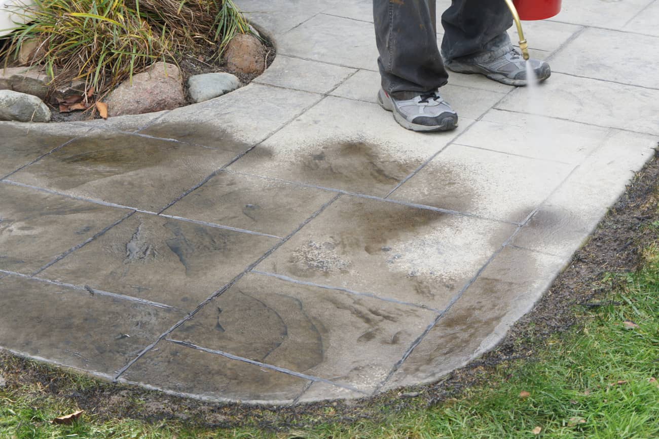 Gebruiker die buiten gestempeld beton in zijn tuin schoonmaakt
