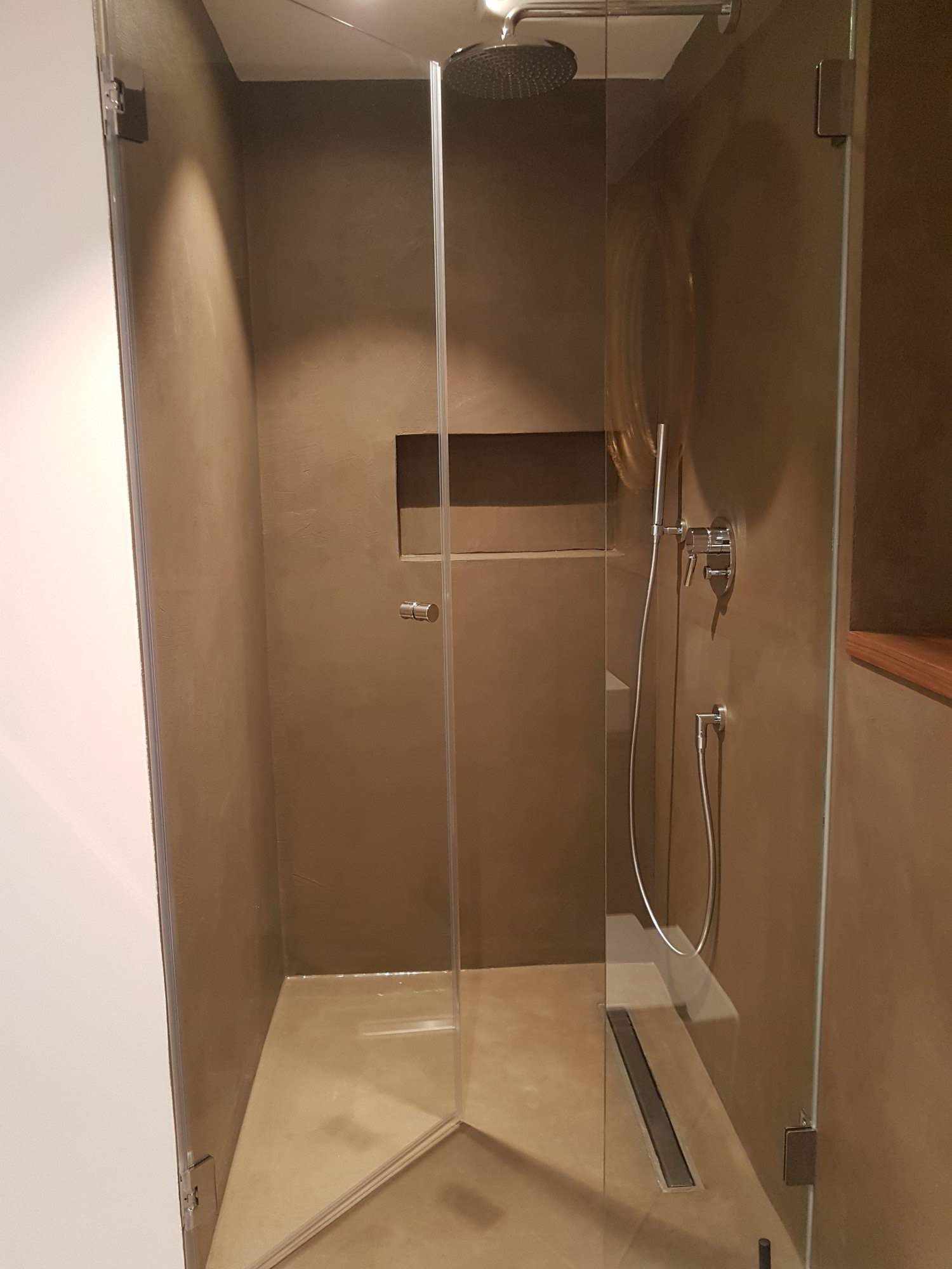 Lichte microcement bekleding in een douche met ingebouwde plank