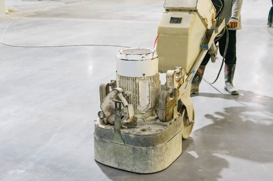 Operator lustruind pavimentul de ciment lustruit cu o mașină de lustruit rotativă.